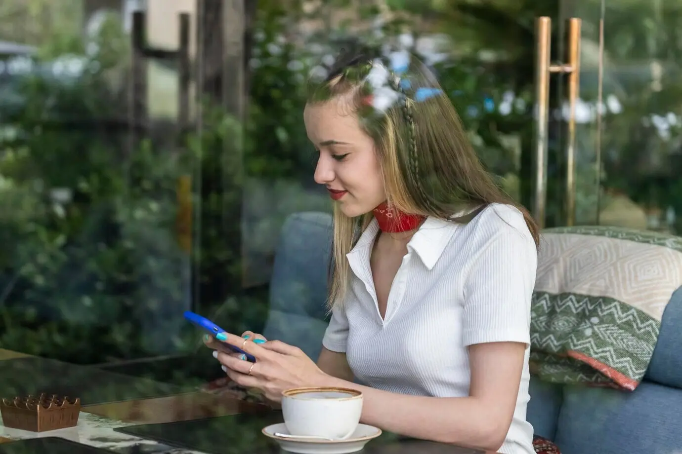 A smiling, beautiful lady is sitting at a restaurant, playing on her phone.