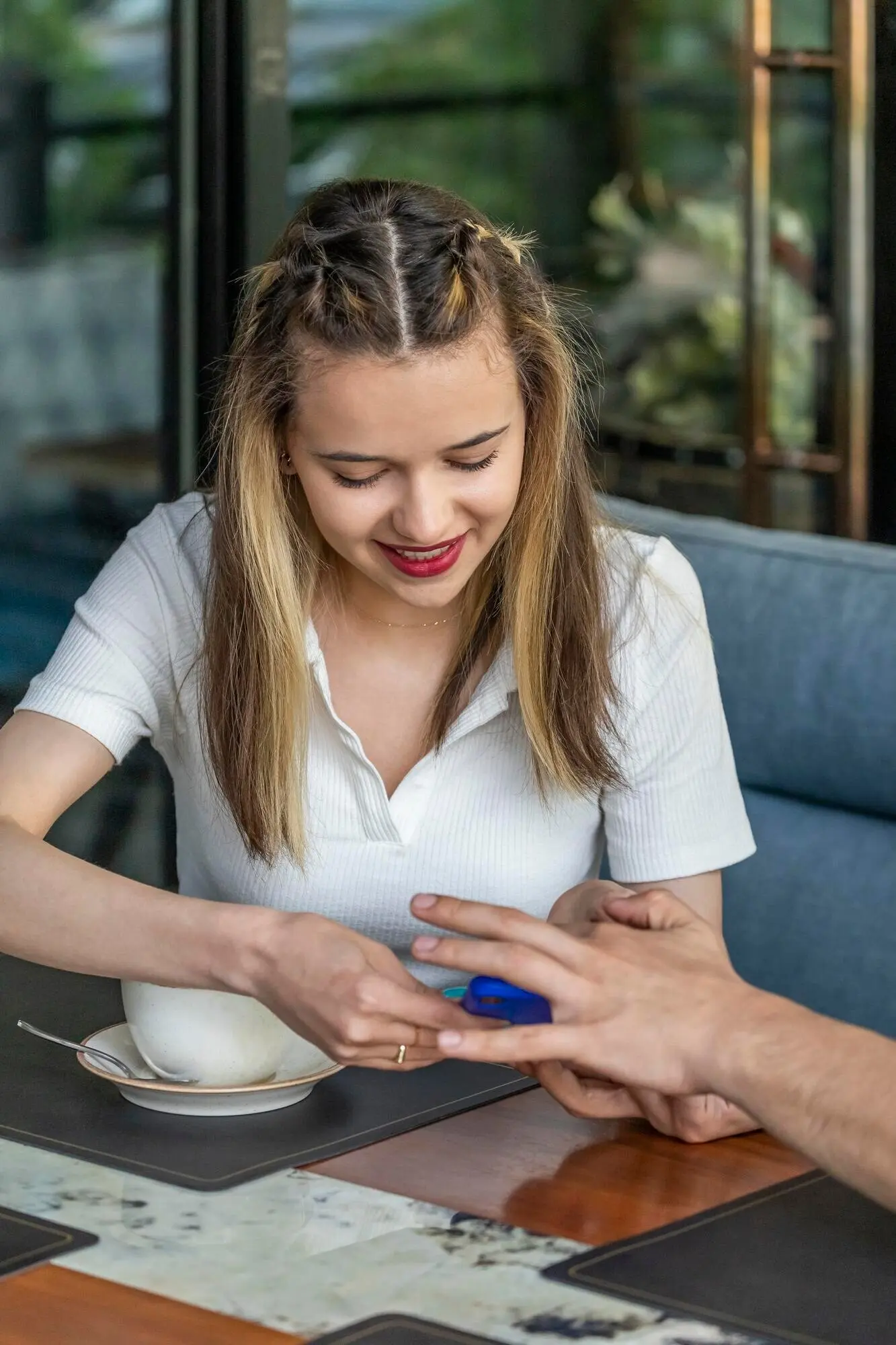 A smiling young girl is sitting in a restaurant, looking at her phone.